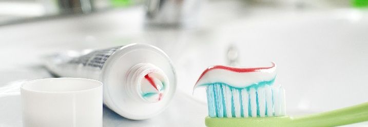 Eine Tube mit bunter Zahnpasta liegt neben einer Zahnbürste auf dem Waschbeckenrand.